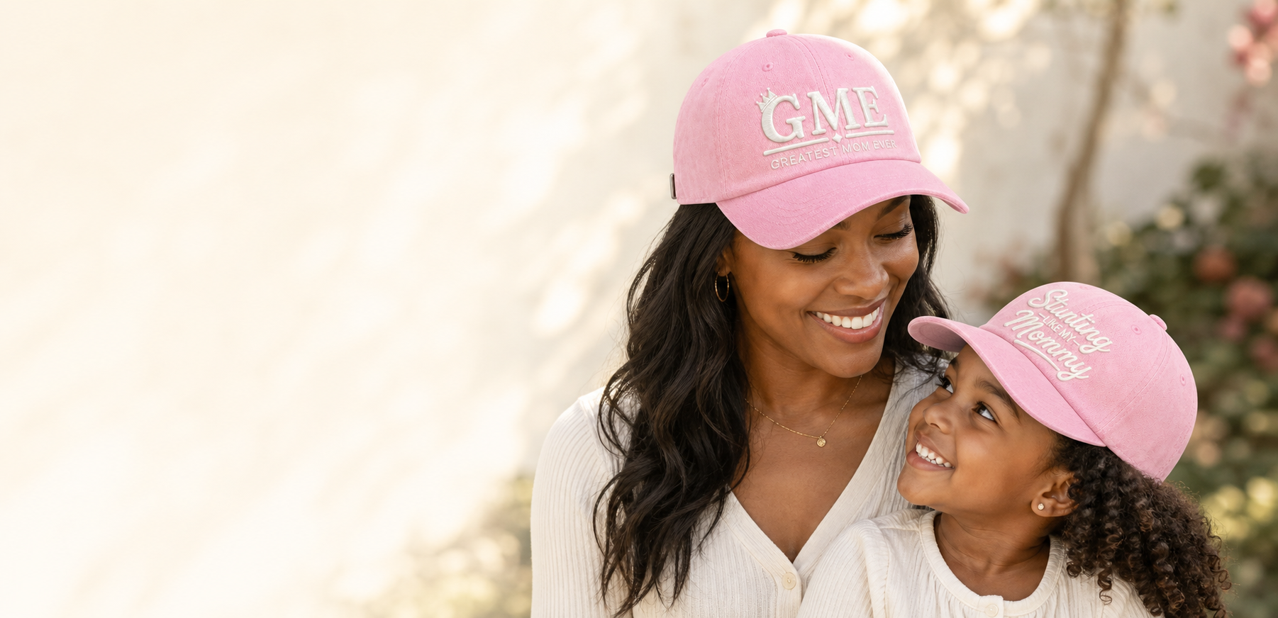 A mother in the GME cap and her daughter in the Stunting Like My Mommy cap, smiling together in warm light