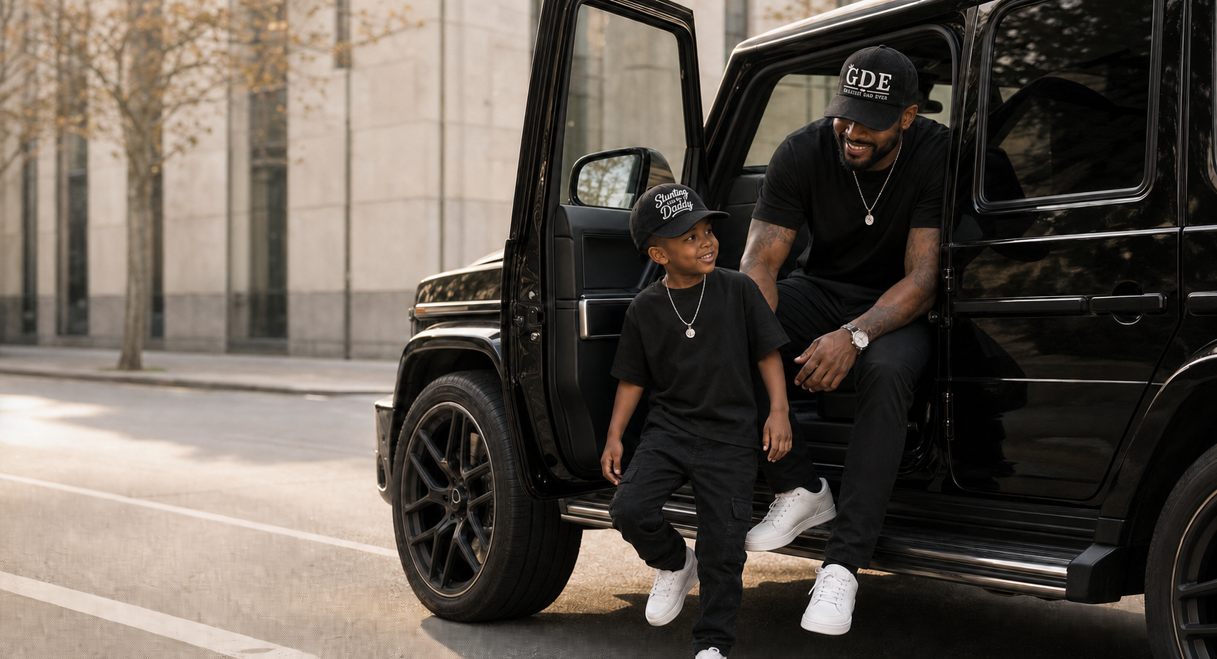 A father in the GDE cap and his son in the Stunting Like My Daddy cap, both in black, beside a black SUV